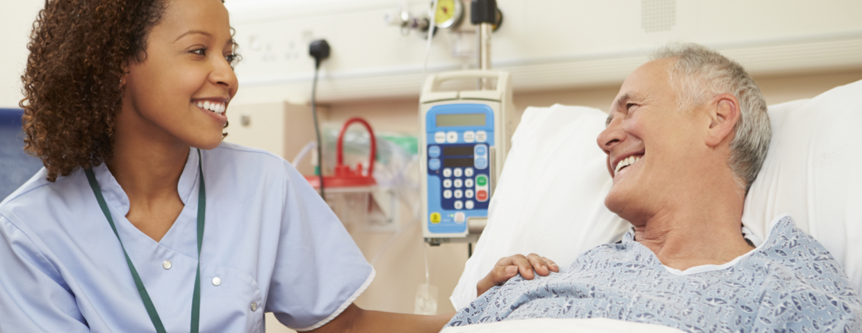 Nurse Sitting By Male Patient's Bed In Hospital